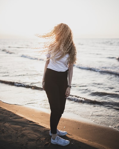 During the day, wearing a white shirt and black pants of woman standing on the beach
